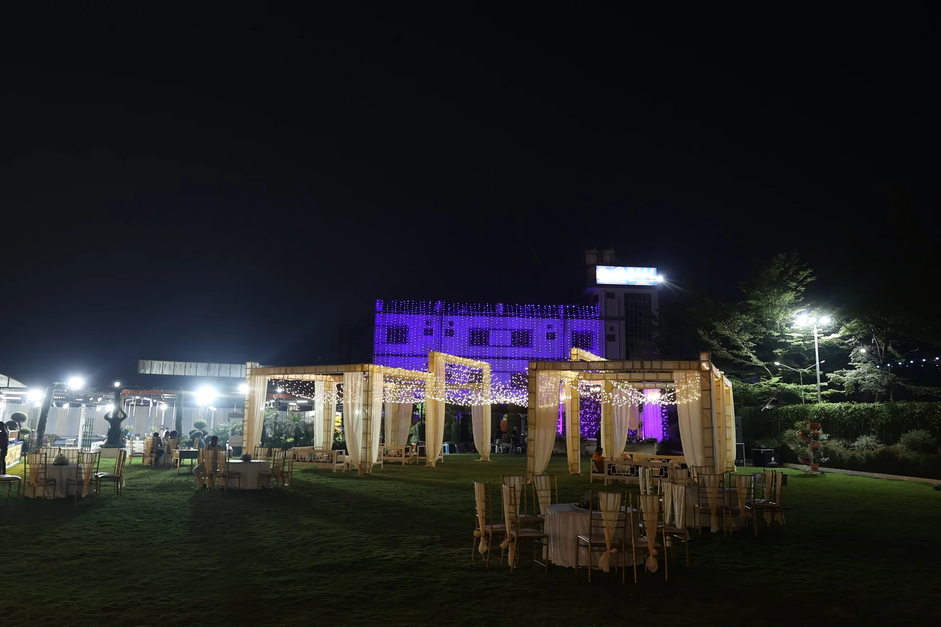 An expansive night view of the Bhandari Farms lawn and illuminated pavilions